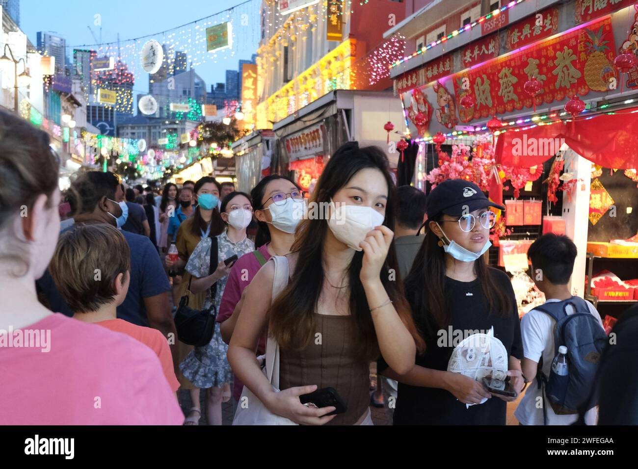 Le ragazze in maschera camminano attraverso un vivace mercato nella Chinatown di Singapore prima del capodanno lunare Foto Stock