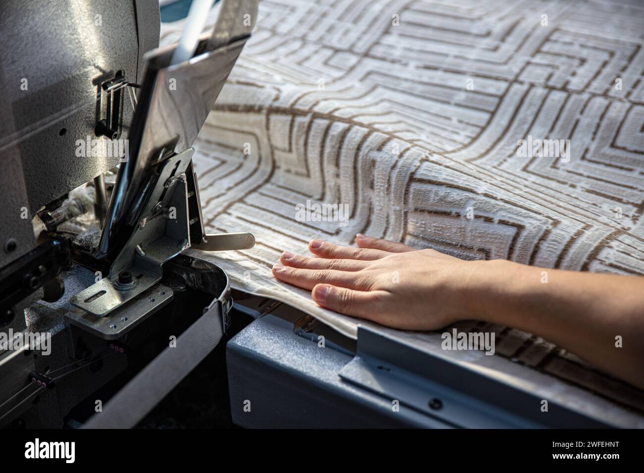 Overlocking del bordo della moquette nella fabbrica di tessitura della moquette. Operaio che ricopre il bordo del tappeto su una macchina da cucire industriale. Foto Stock