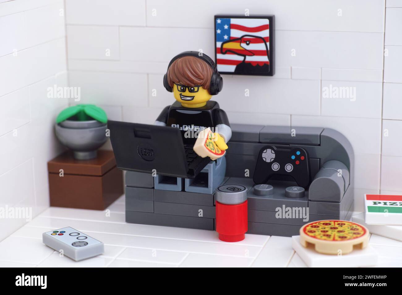 Tambov, Federazione Russa - 30 gennaio 2024 Un personaggio di un videogioco Lego seduto su un divano, che gioca a videogiochi su un computer portatile e mangia una pizza. Foto Stock