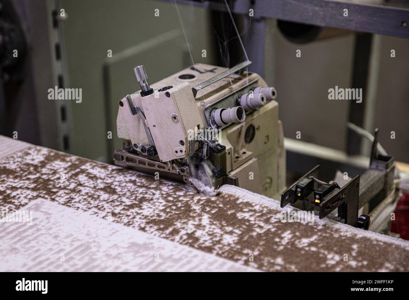 Overlocking del bordo della moquette nella fabbrica di tessitura della moquette. Operaio che ricopre il bordo del tappeto su una macchina da cucire industriale. Foto Stock