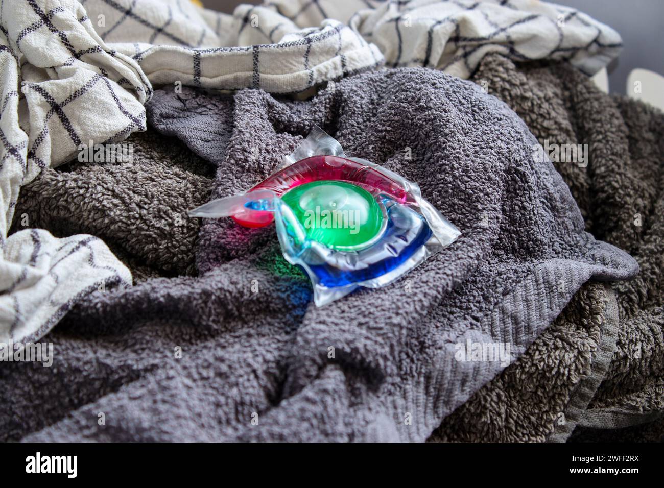 Gel detergente ecologico colorato in capsula su bucato in un cestello Foto Stock