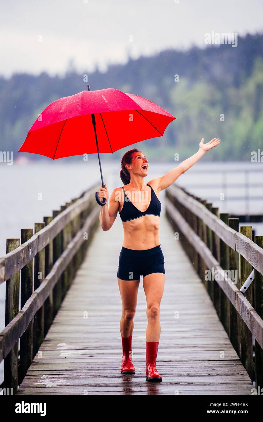Donna con ombrello sul molo che indossa abiti da ginnastica Foto Stock
