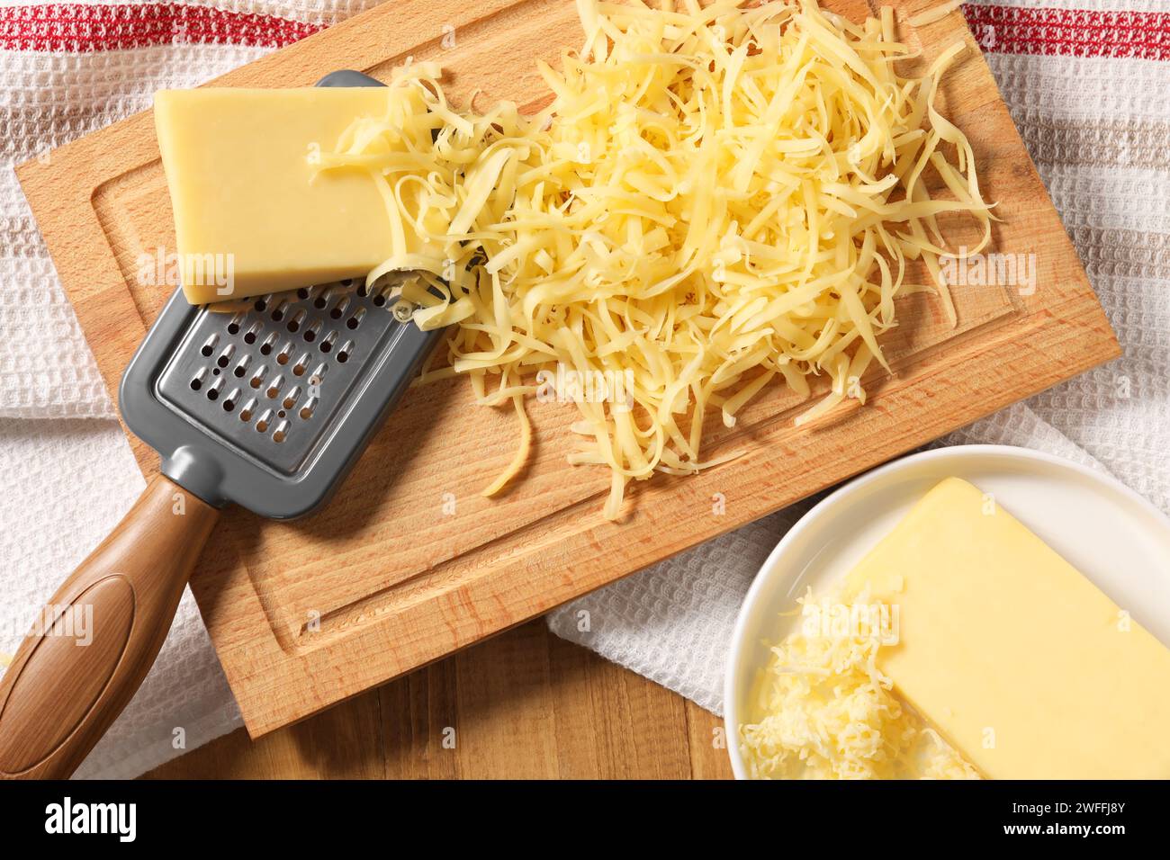 Grattugiato, pezzi interi di formaggio e grattugia su un tavolo di legno, vista dall'alto Foto Stock