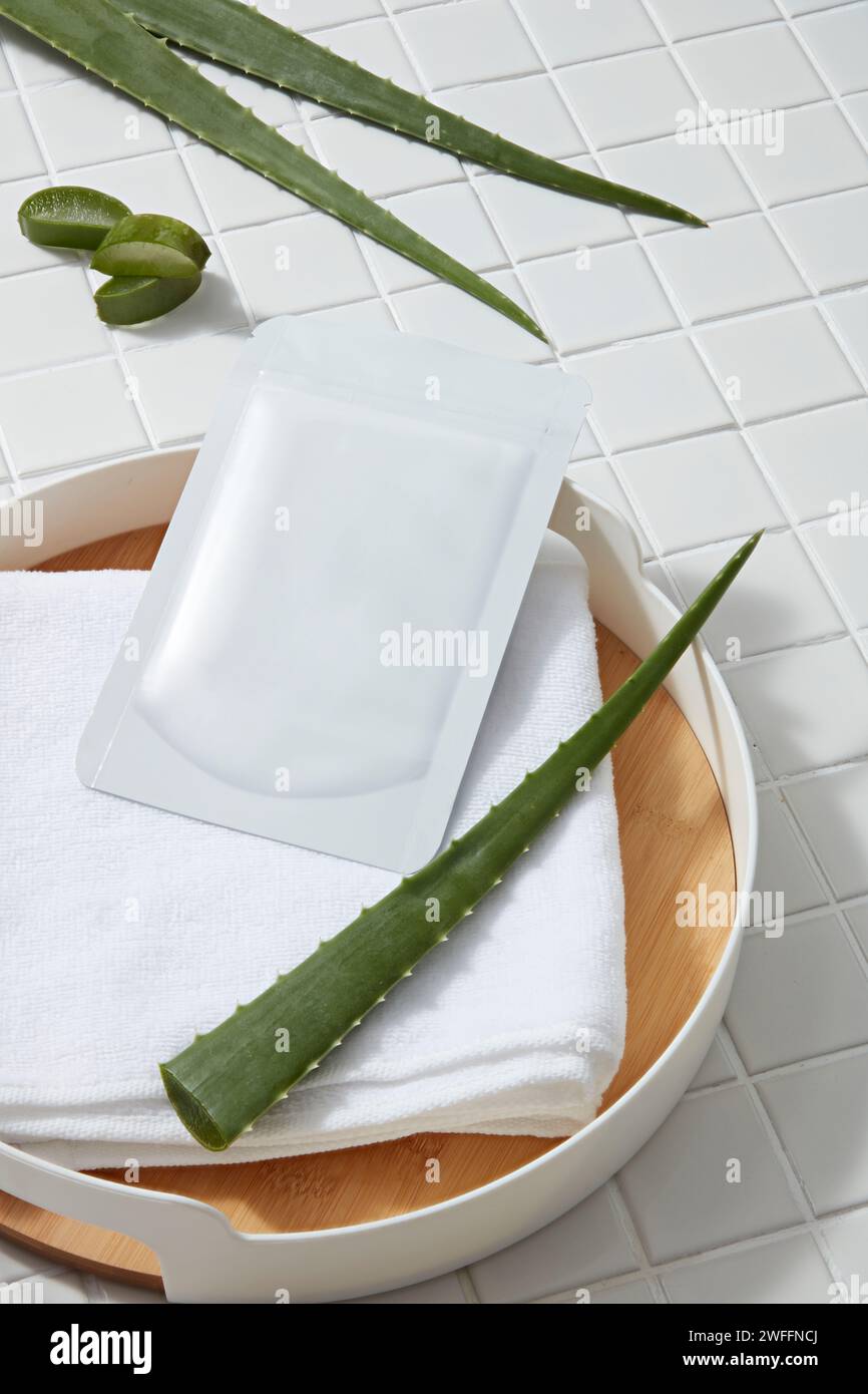 Un foglio maschera non etichettato inserito su un asciugamano all'interno di un vassoio con aloe vera fresca. L'aloe vera (Aloe barbadensis miller) è ricca di antiossidanti e minerali Foto Stock