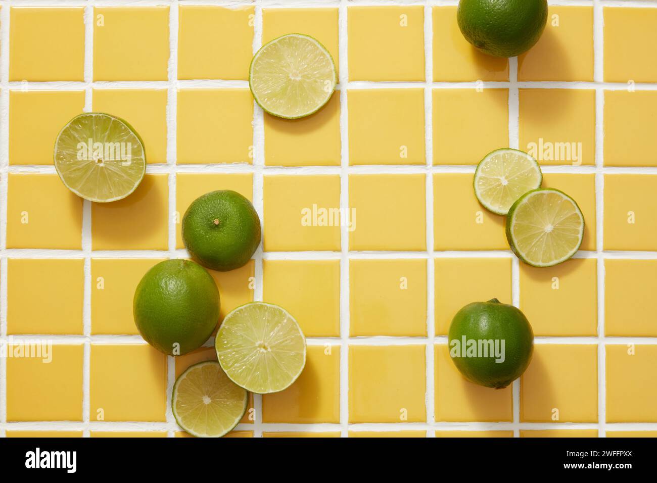 La scena minimale di diverse fette di lime e lime è decorata su uno sfondo di tessere a mosaico giallo. Spazio vuoto per la presentazione del prodotto cosmetico di Lime (. Foto Stock