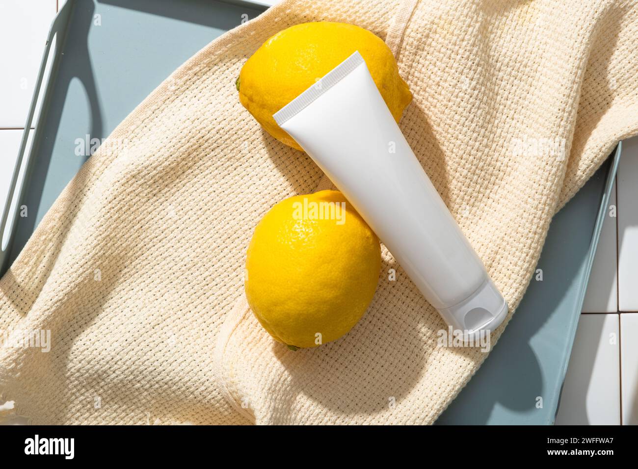 Un vassoio pastello con un asciugamano e una provetta bianca con etichetta vuota visualizzata su. La vitamina C del Limone (Citrus limon) è essenziale per la produzione di collagene. Foto Stock