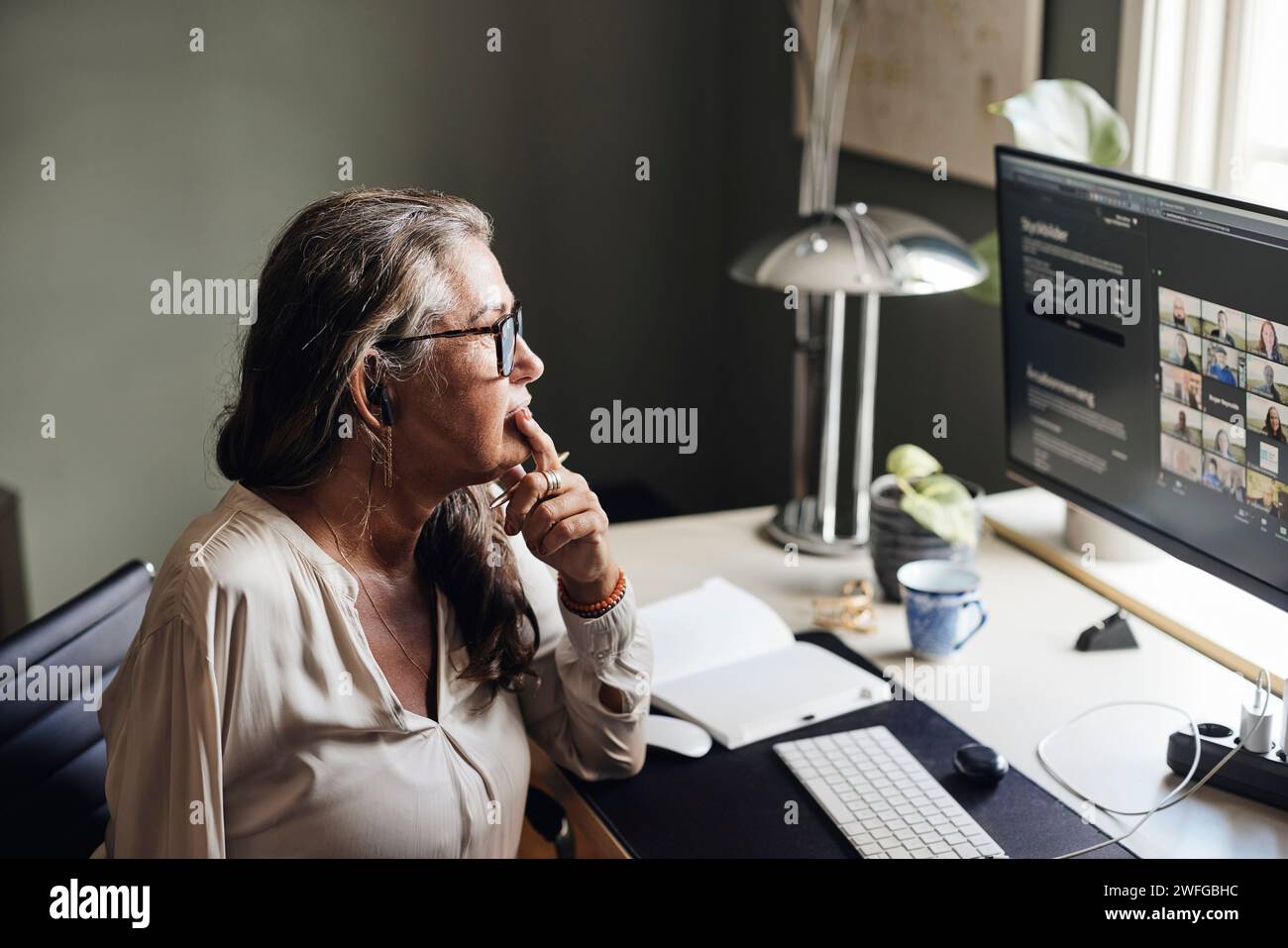 Donna d'affari con la mano sul mento durante la videoconferenza sul computer in ufficio domestico Foto Stock