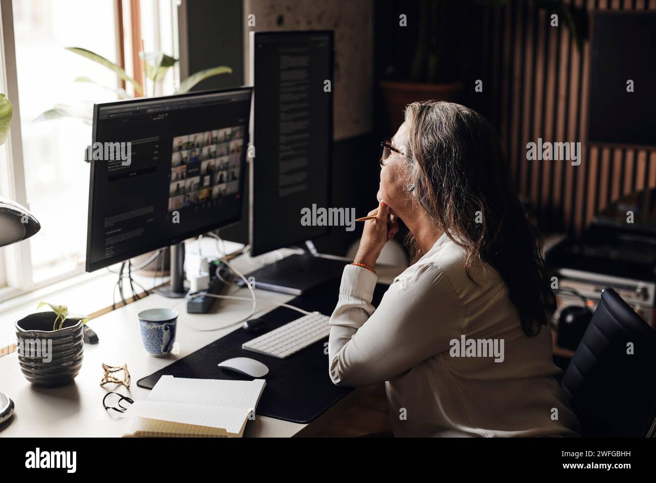 Donna d'affari con la mano sul mento che fa videoconferenze al computer mentre è seduta in ufficio Foto Stock
