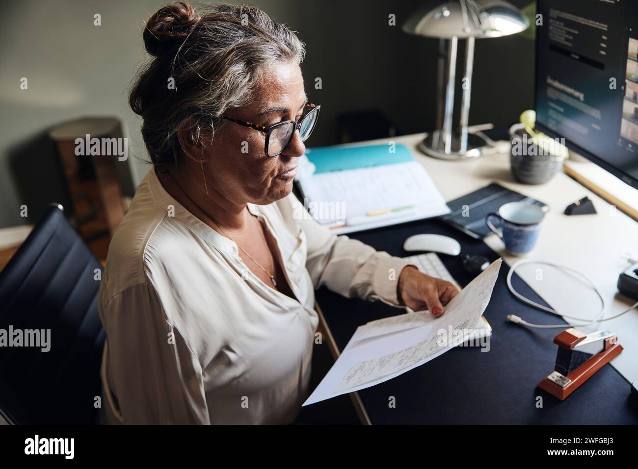 Donna matura freelance che esamina i documenti alla scrivania in ufficio Foto Stock