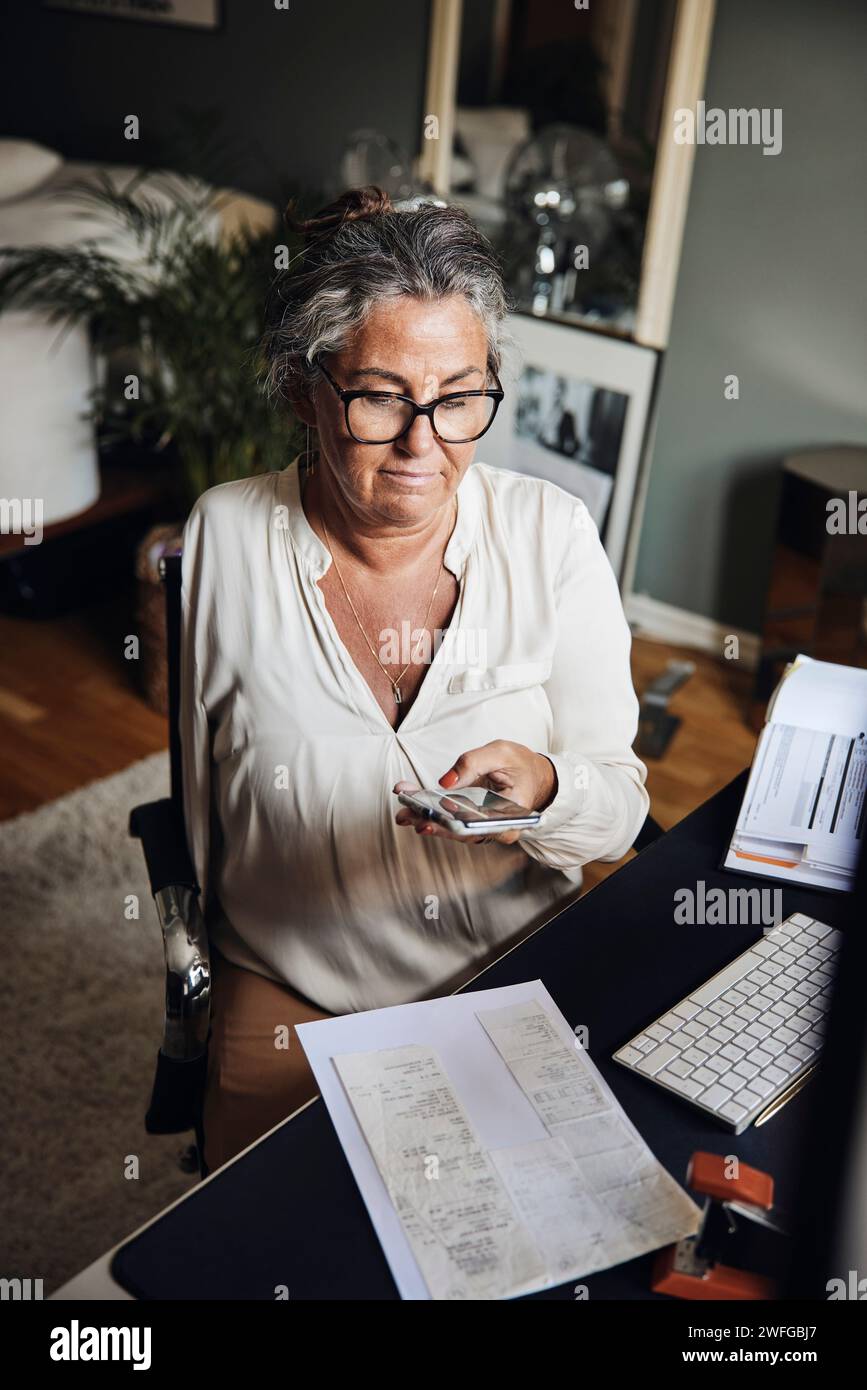 Donna d'affari con disabilità che fotografa documenti mentre è seduta alla scrivania in ufficio Foto Stock