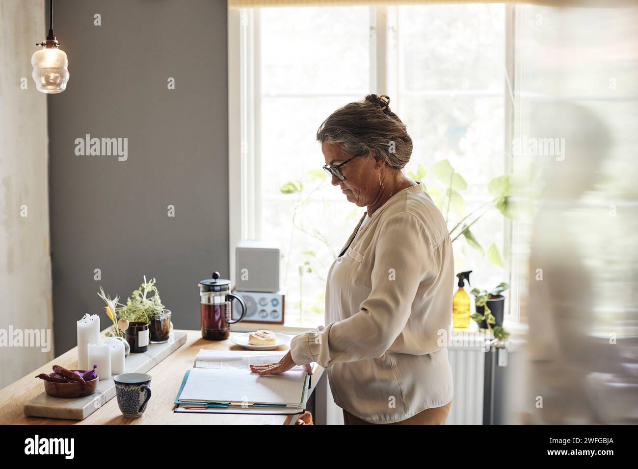 Vista laterale di una donna che esamina le bollette finanziarie mentre è in cucina a casa Foto Stock
