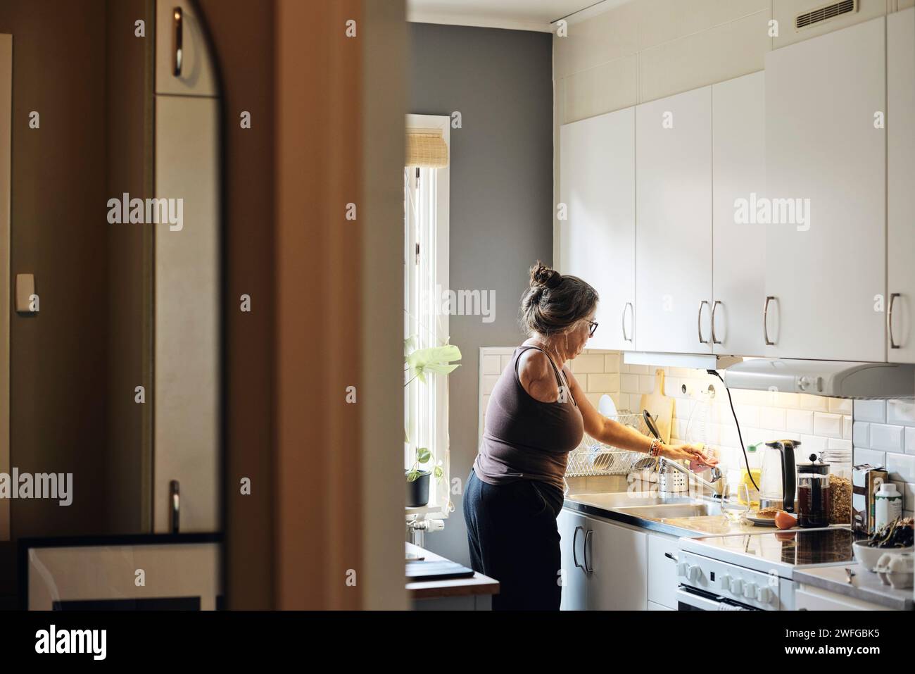 Vista laterale della donna con disabilità che spegne il rubinetto mentre lavora in cucina a casa Foto Stock