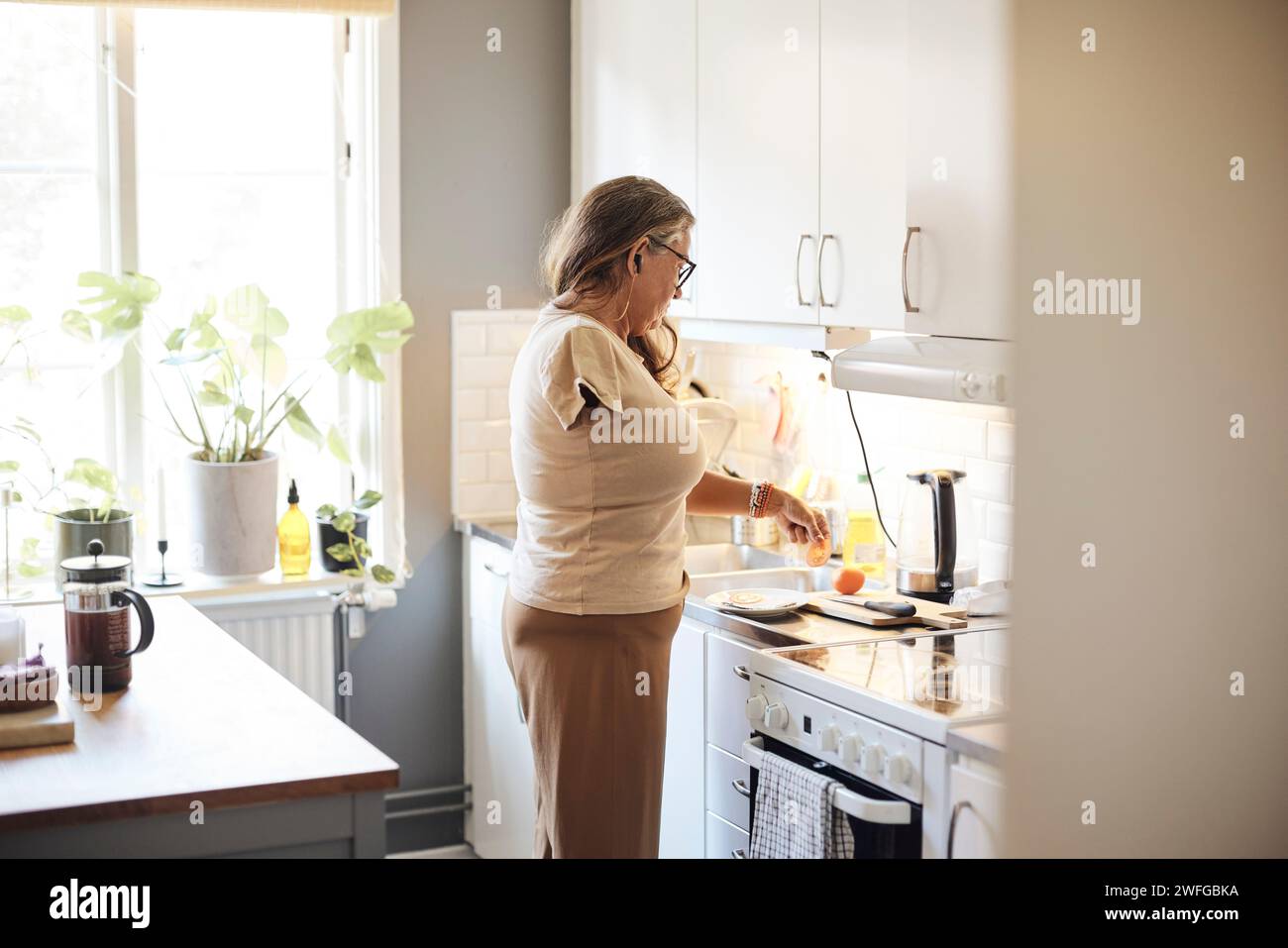 Vista laterale di una donna matura con disabilità che prepara la colazione in cucina a casa Foto Stock