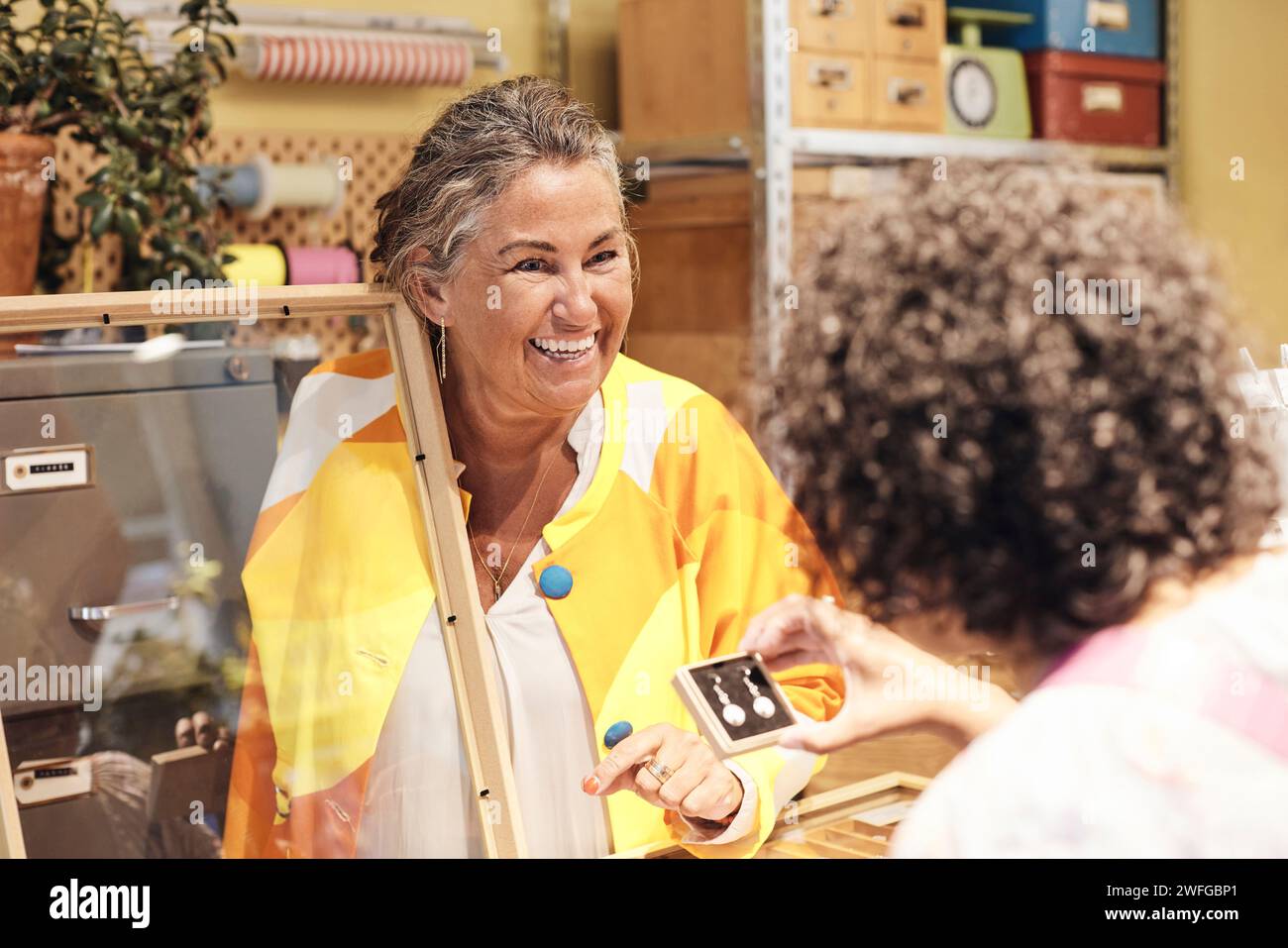Donna di vendita felice che assiste una cliente donna che acquista un orecchino in negozio Foto Stock