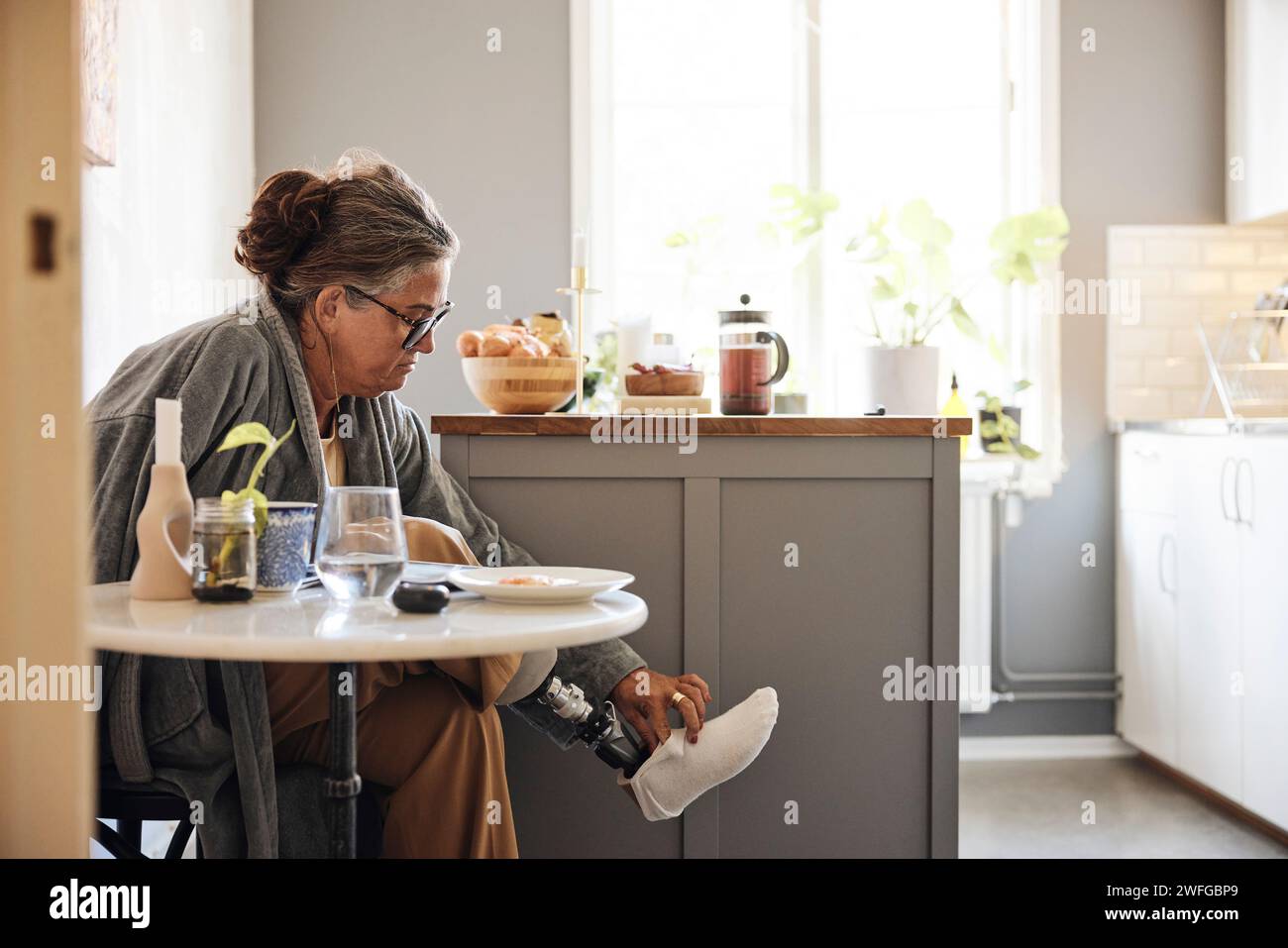 Donna matura che indossa una gamba protesica mentre è seduta a casa Foto Stock