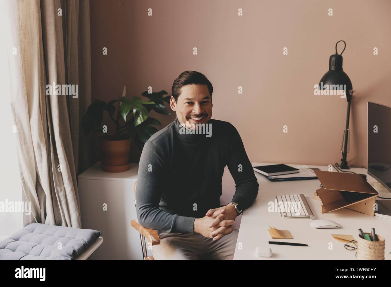 Ritratto di un professionista maschile sorridente seduto alla scrivania in ufficio Foto Stock