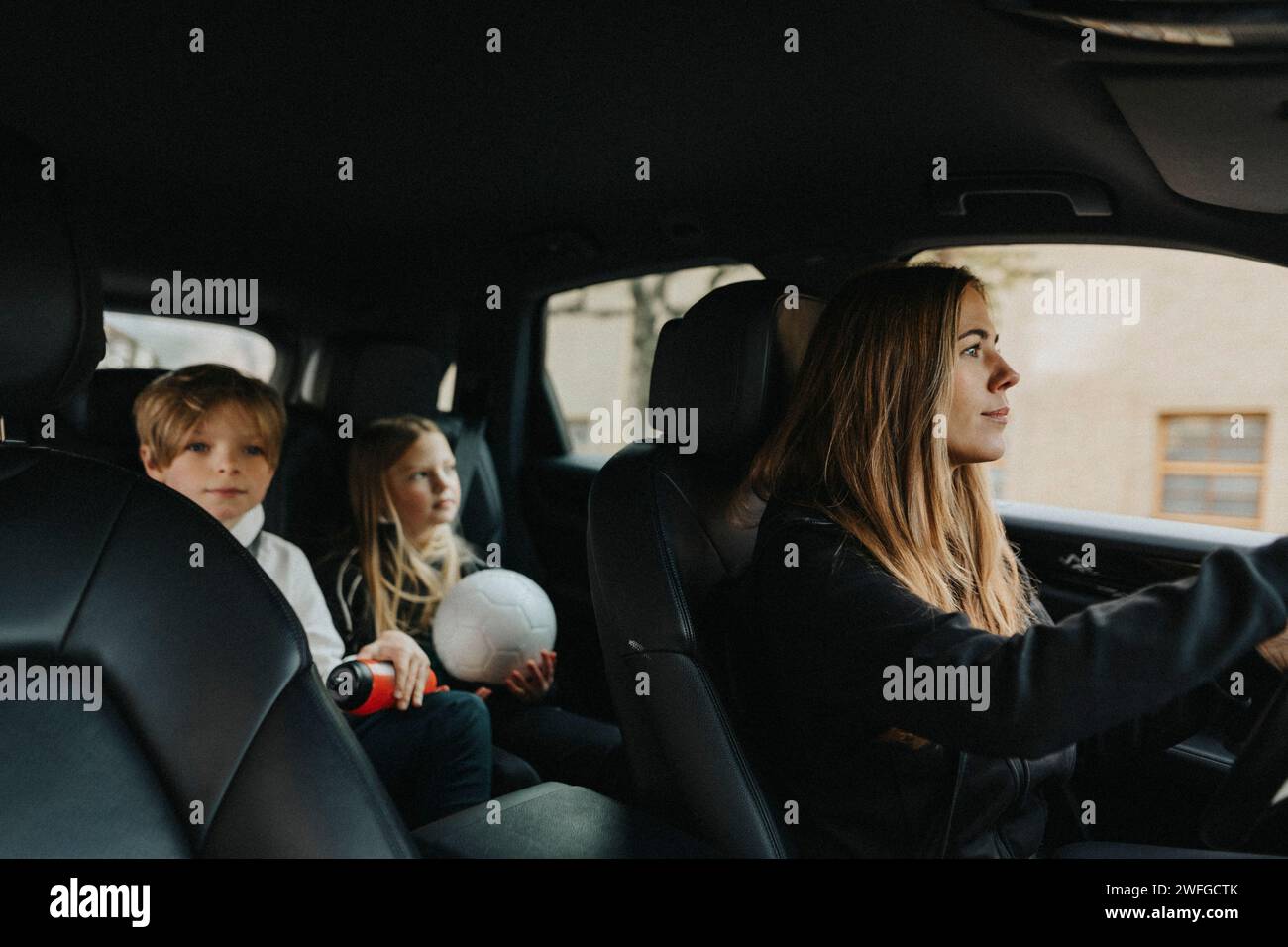 La madre guida mentre il figlio e la figlia sono seduti in macchina durante il viaggio del fine settimana Foto Stock