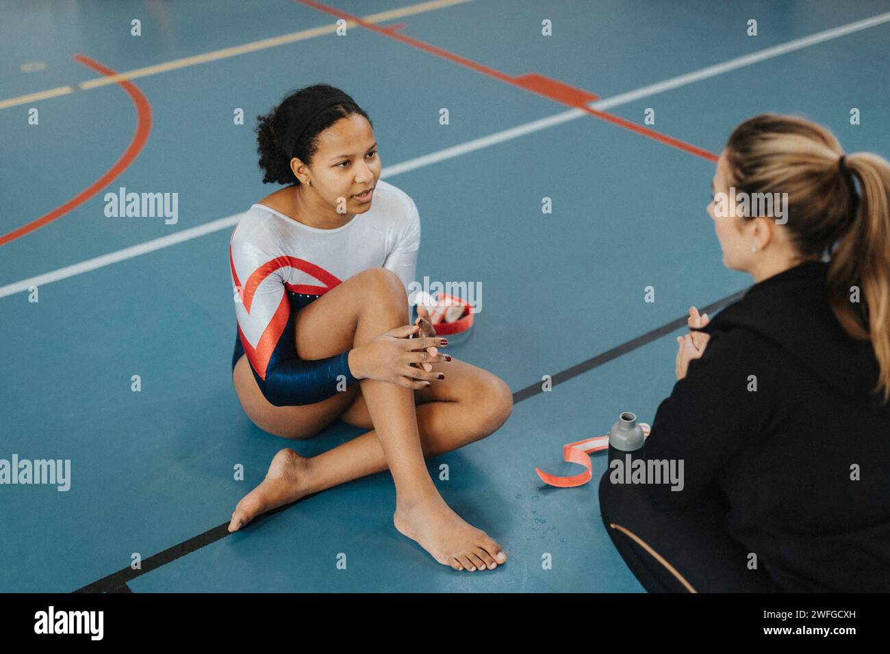 Atleta che prende consigli dal coach mentre si siede in palestra Foto Stock