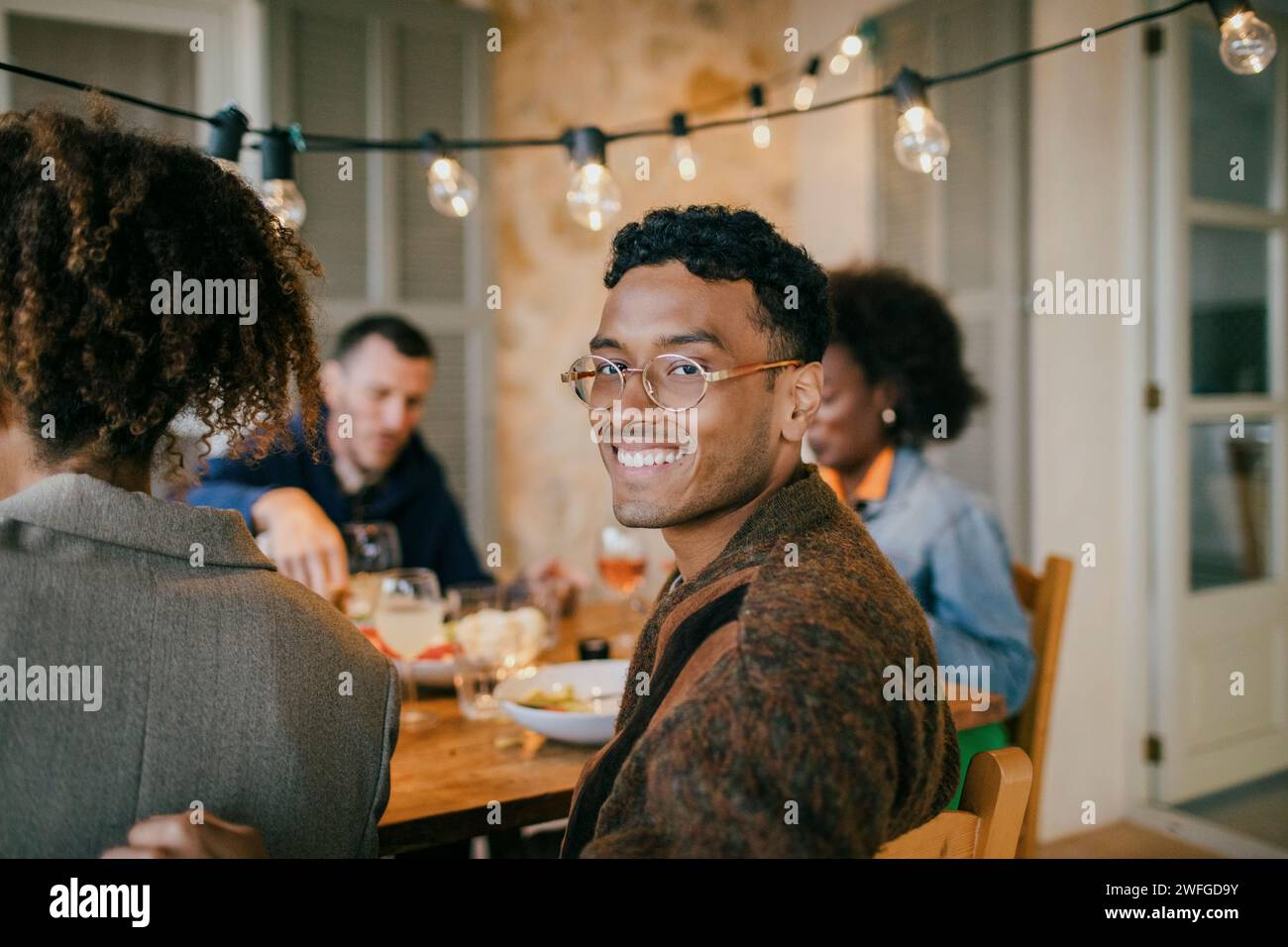 Ritratto di un giovane sorridente che indossa occhiali da vista seduto nel patio durante la cena Foto Stock