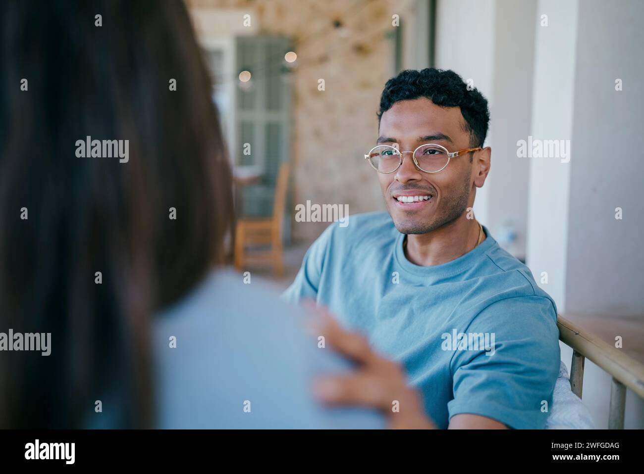 Un giovane sorridente che parla con una donna seduta nel patio Foto Stock