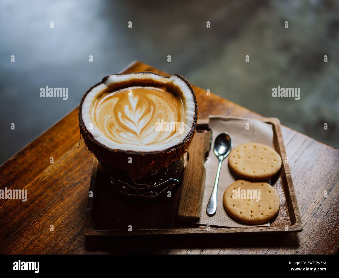 Caffè latte caldo al cocco. Vassoio con una tazza di gustoso caffè al cocco. Tazza di gustoso caffè al cocco e cucchiaio con cracker su tavolo di legno. Caldo caffè lat Foto Stock