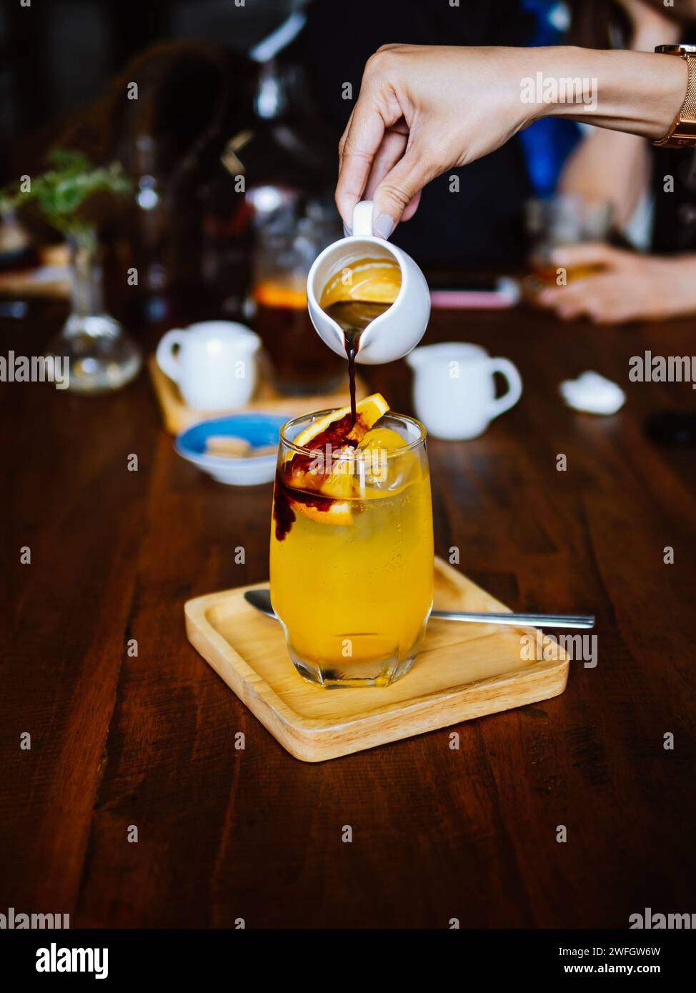 Bere una bevanda fredda rinfrescante con succo d'arancia appena spremuto, espresso e ghiaccio in preparazione. Versare del caffè nero nel bicchiere riempito Foto Stock