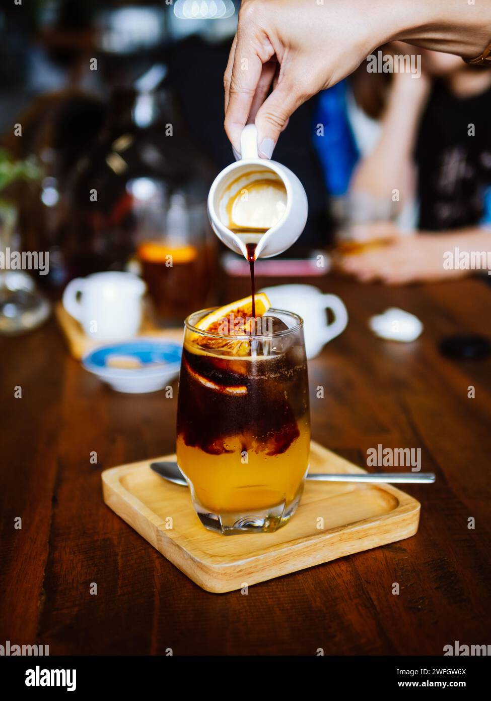 Bere una bevanda fredda rinfrescante con succo d'arancia appena spremuto, espresso e ghiaccio in preparazione. Versare del caffè nero nel bicchiere riempito Foto Stock