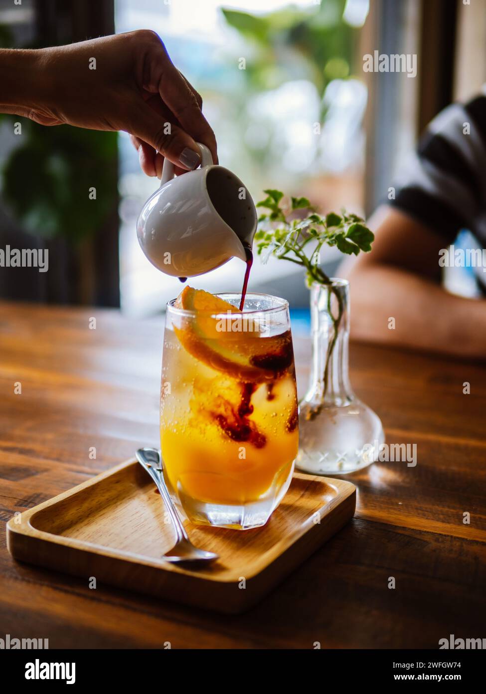 Bere una bevanda fredda rinfrescante con succo d'arancia appena spremuto, espresso e ghiaccio in preparazione. Versare del caffè nero nel bicchiere riempito Foto Stock
