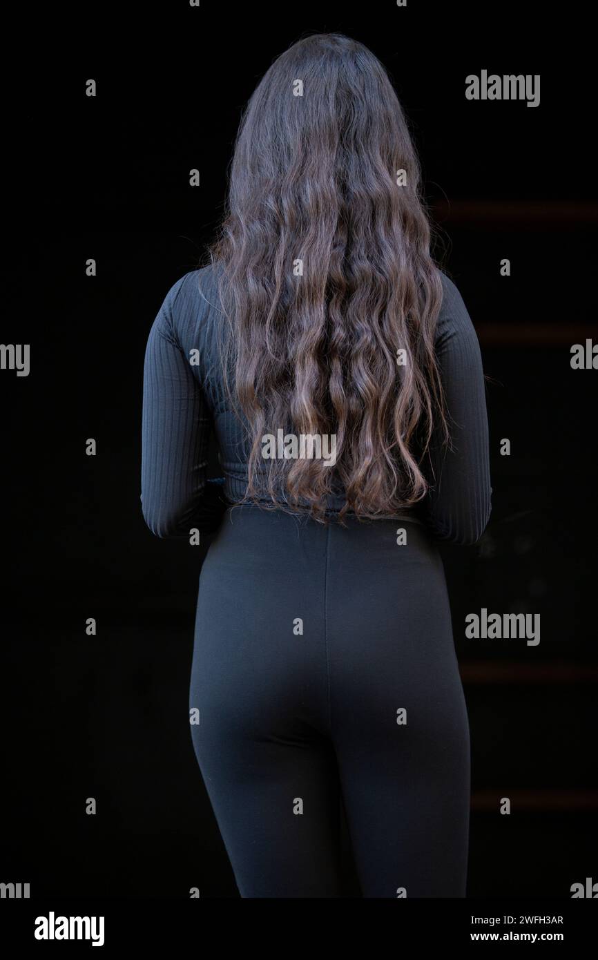 Vista posteriore di una donna in nero su sfondo nero Foto Stock