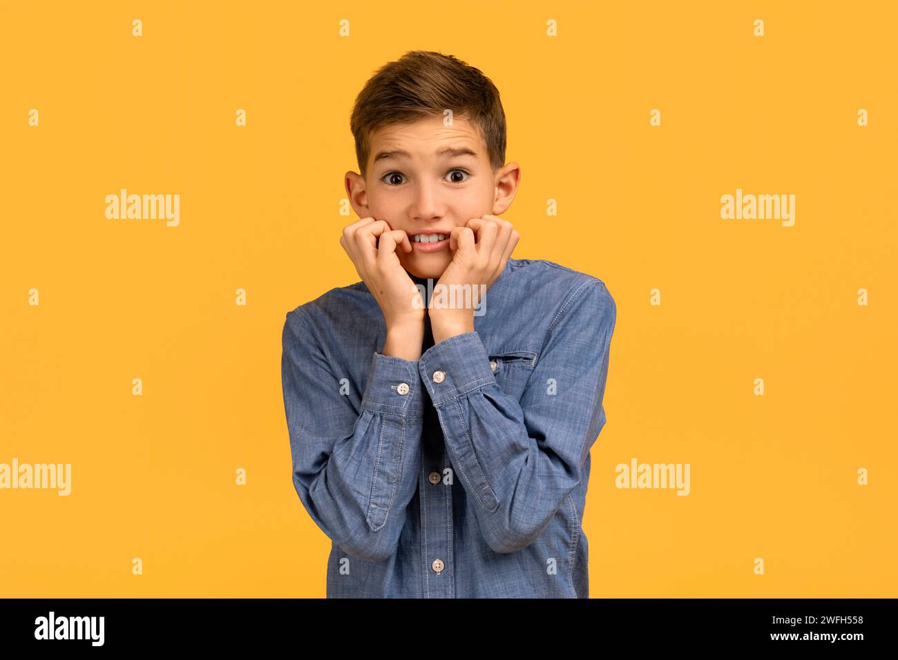Teenager ansioso con camicia in denim che morde le unghie e guarda la macchina fotografica Foto Stock