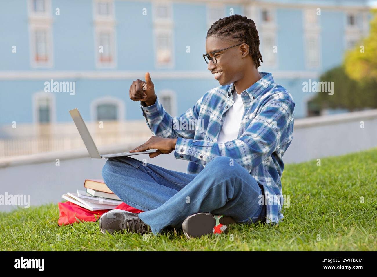 Il ragazzo nero che gestiva i pollici fino alla webcam del computer portatile seduto all'aperto Foto Stock