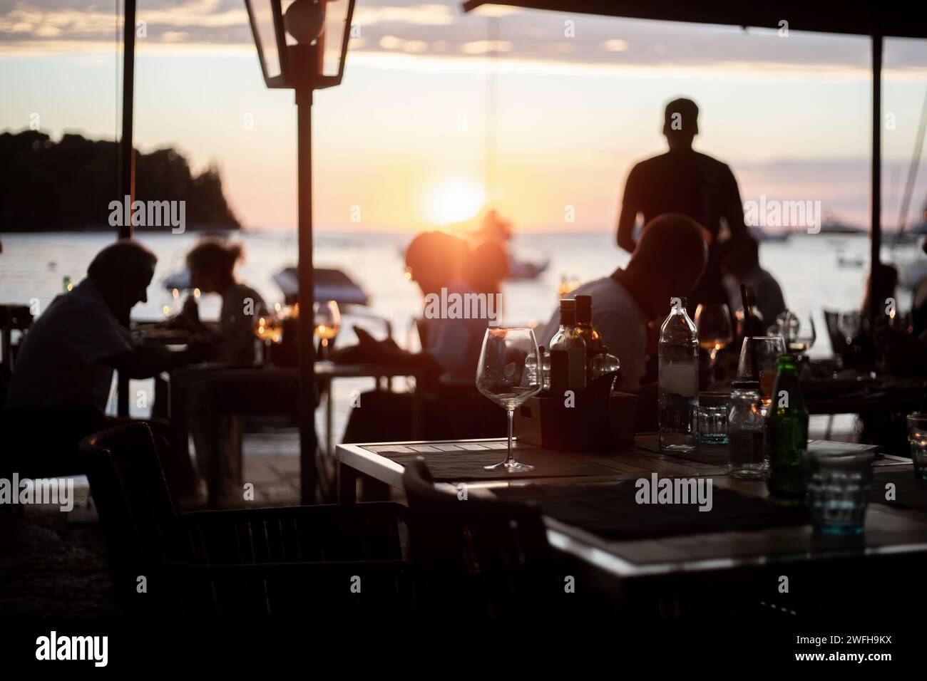 persone che cenano al ristorante sul mare con un tramonto romantico Foto Stock