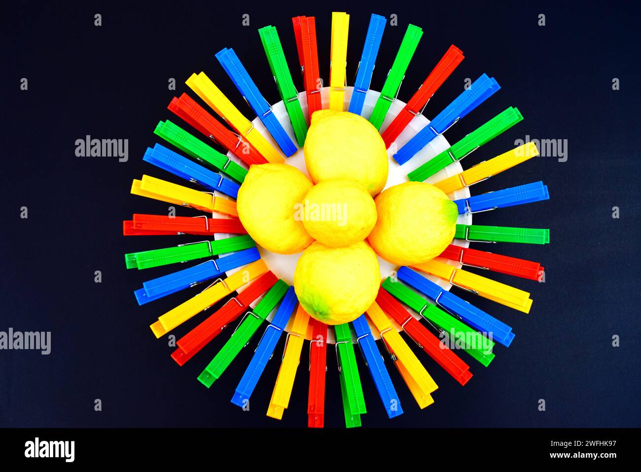Un cerchio rotondo, fatto di clothespins di plastica colorata e una pila di limoni freschi seduti al centro. Foto Stock