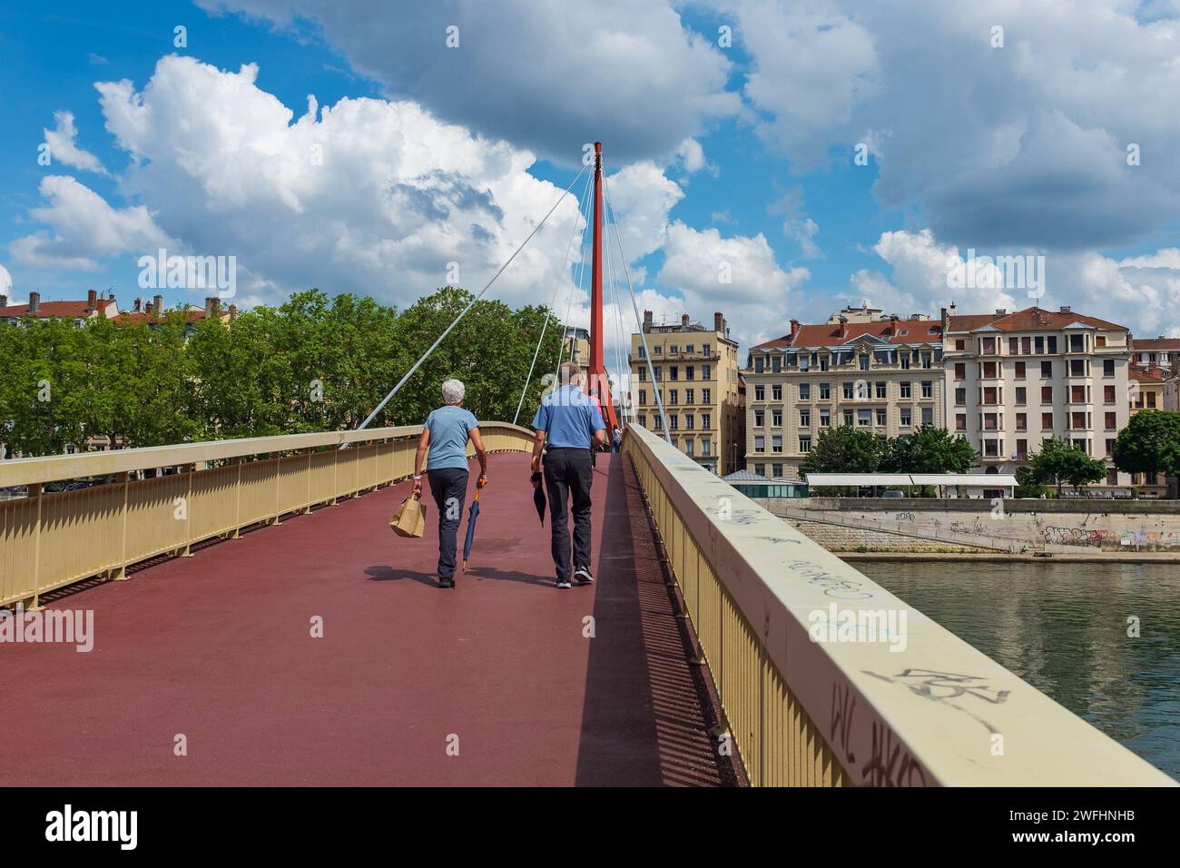 Lione, Francia, 2023. Un'energica coppia anziana che attraversa il ponte del Palais de Justice, con il Presqu'île (secondo arrondissement) sullo sfondo Foto Stock