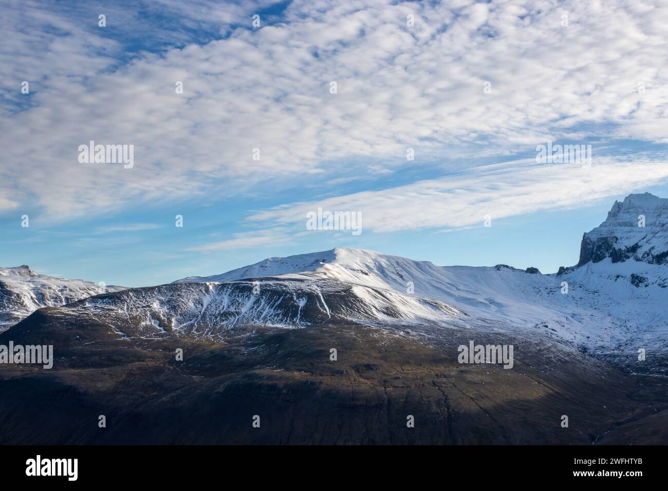 Vista da una valle, circondata da montagne con un leggero strato di neve. Cielo blu con nuvole bianche strutturate. Borgarfjordur, Islanda nordorientale. Foto Stock