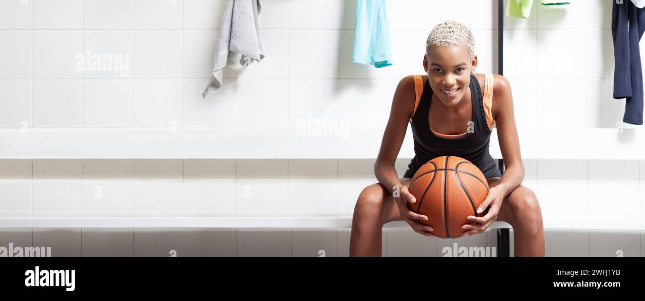 Pallacanestro sportivo nello spogliatoio, un'atleta afroamericana sorridente che tiene la palla prima della partita, della competizione o dell'allenamento. Donna Foto Stock