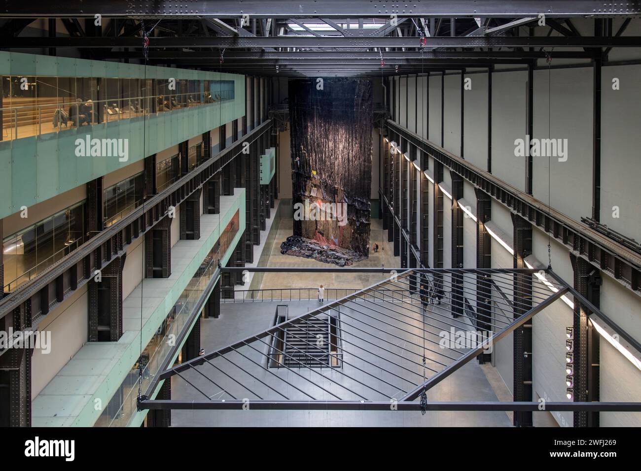 Londra, Regno Unito - 12 dicembre 2023; turbine Hall of Tate galleria d'arte moderna con opere d'arte di impiccagioni in metallo a cascata dietro la Luna Rossa dell'artista El Anatsu Foto Stock