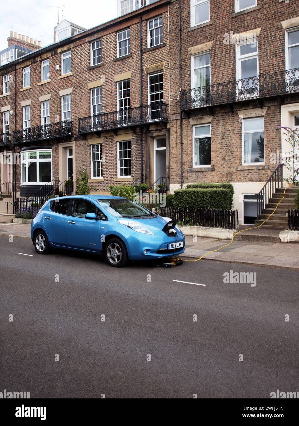 Una "Blue Nissan Leaf Saloon car" con unità batteria del veicolo caricata dai proprietari di alimentazione elettrica domestica in strada. Foto Stock