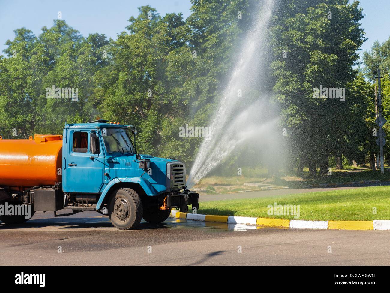 Il camion spruzza l'acqua su un prato verde della città. Economia urbana. Miglioramento delle aree verdi. Foto Stock