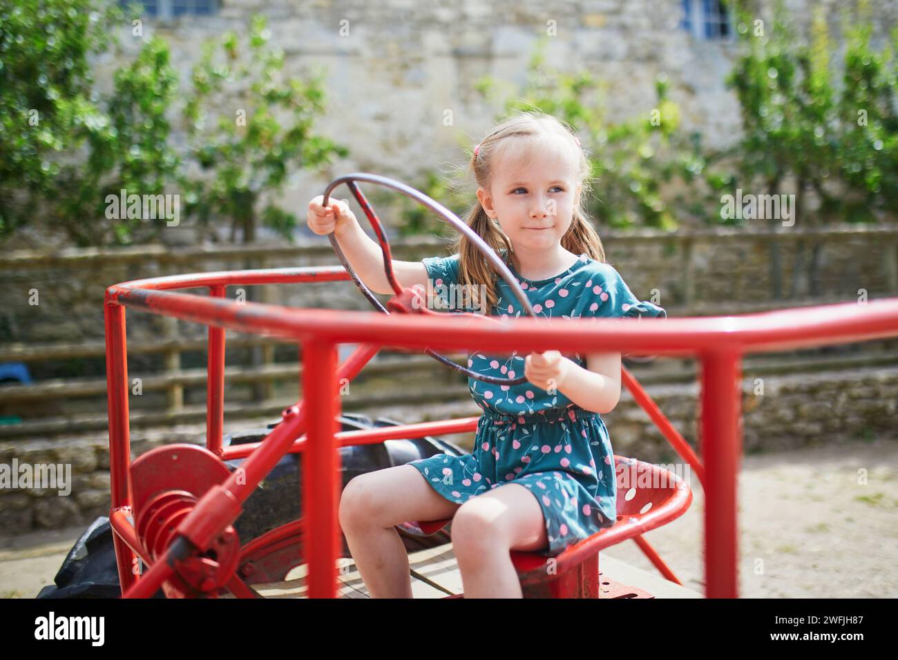 Adorabile bambina in età prescolare che gioca su un vecchio trattore rosso nella fattoria Gally vicino a Parigi, in Francia. Attività estive all'aperto per bambini Foto Stock