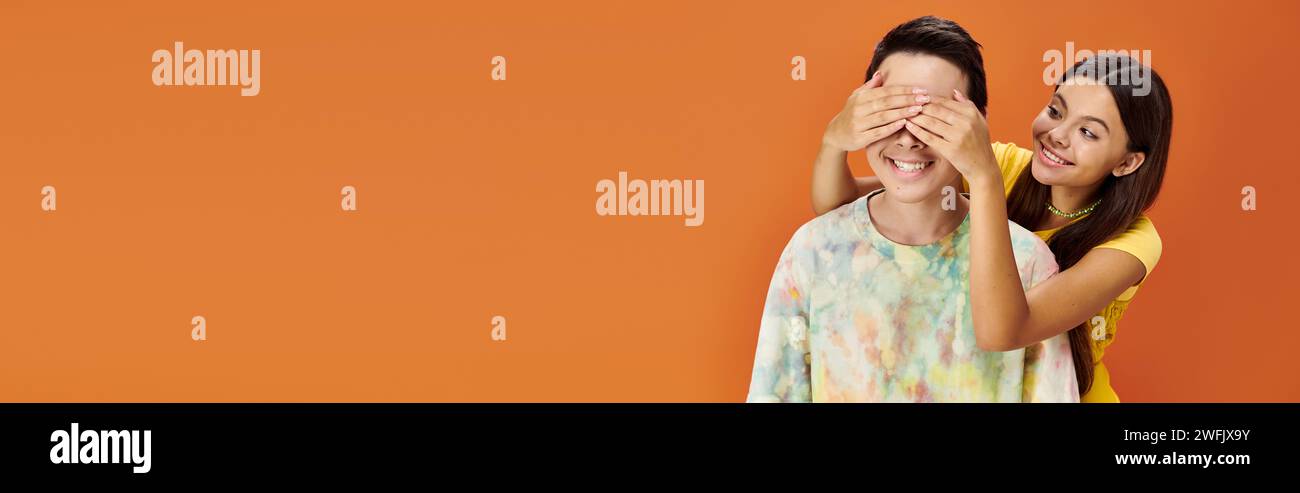 bella ragazza adolescente che chiude gli occhi della sua amica asiatica su sfondo arancione, giorno dell'amicizia, striscione Foto Stock