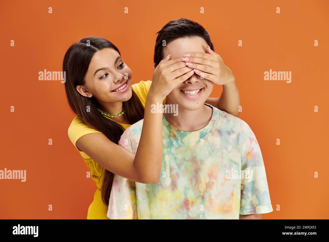 jolly bruna adolescente che chiude gli occhi del suo amico asiatico su sfondo arancione, giorno dell'amicizia Foto Stock