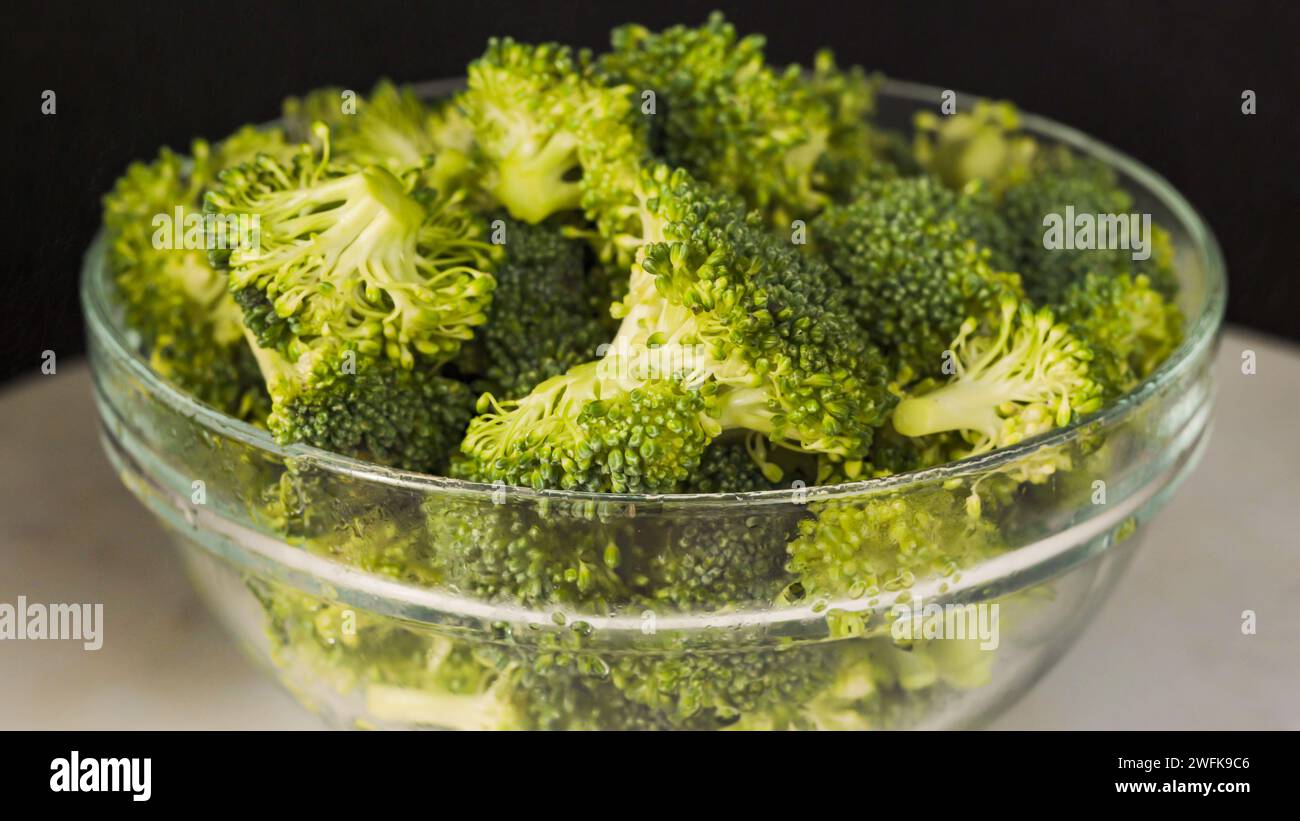 Una ciotola di vetro con broccoli biologici crudi in primo piano su sfondo nero Foto Stock