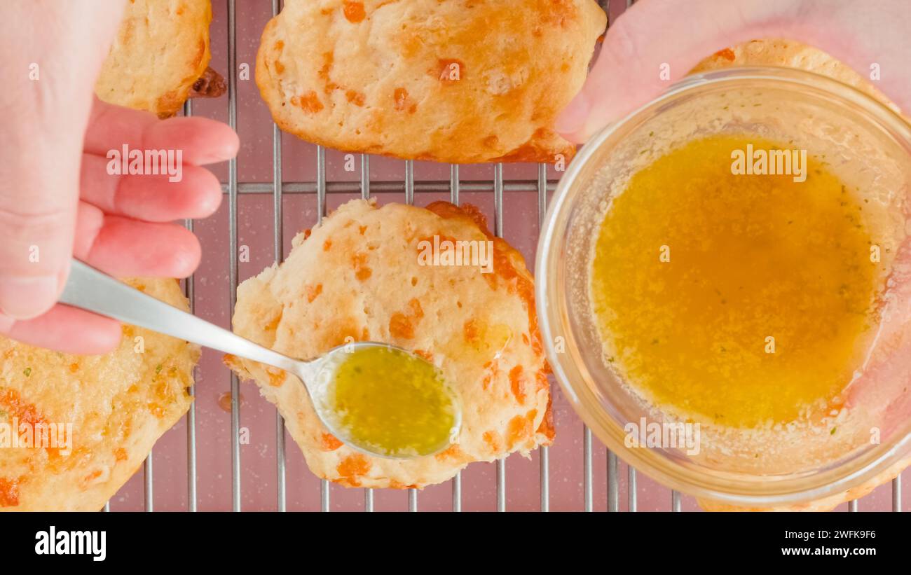 Ricetta dei biscotti al formaggio, processo di cottura. Donna che condisce biscotti appena sfornati con burro fuso e condimento all'aglio, a base piatta Foto Stock