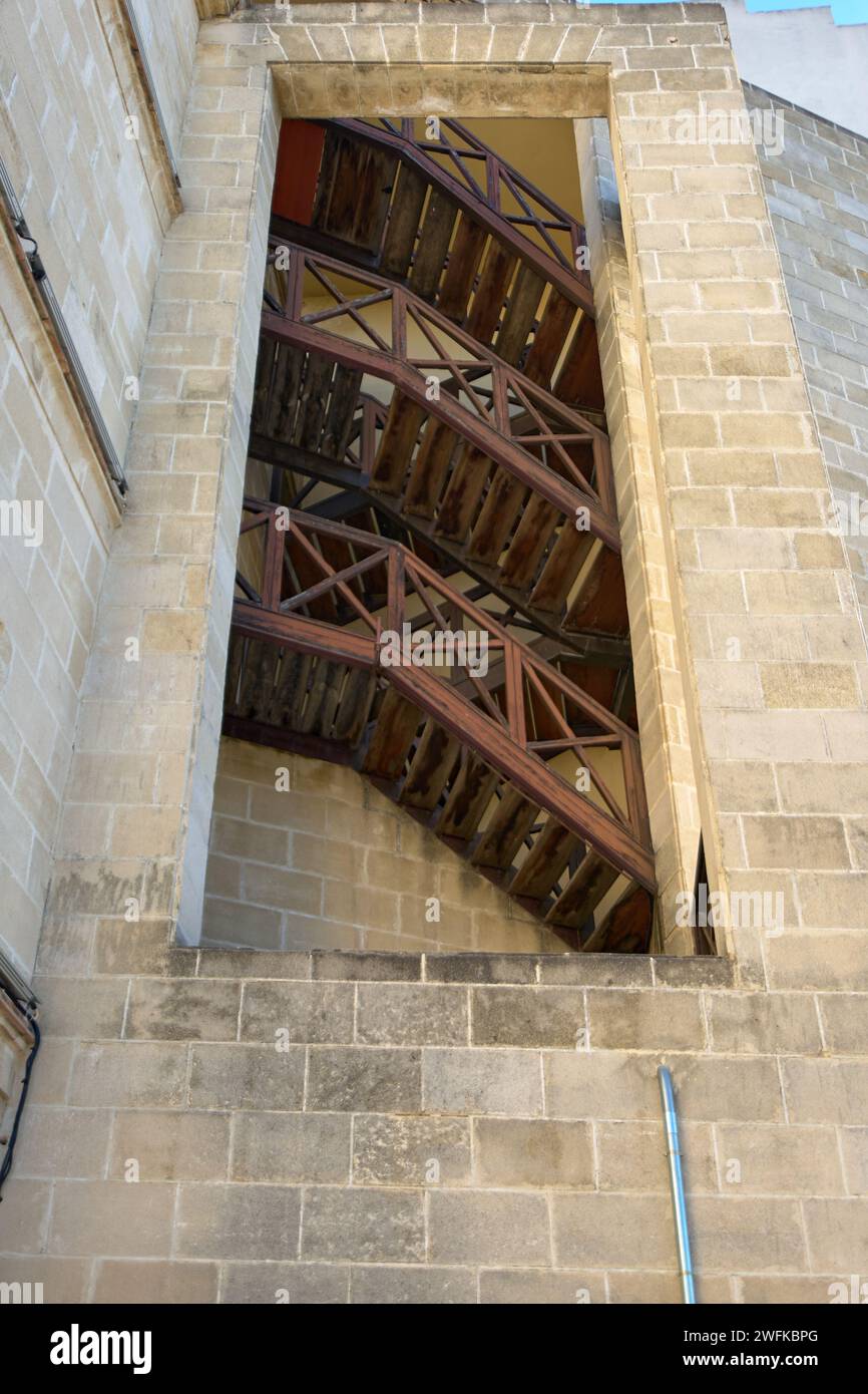 Una vista unica di una scala in legno attraverso una finestra aperta in uno storico edificio in pietra a Jerez de la Frontera Foto Stock