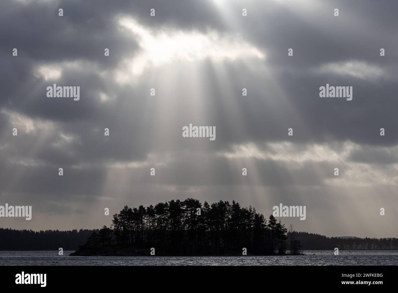 La luce del sole splende attraverso le nuvole grigie sull'isola ricoperta di alberi. Concetto di luce divina. Foto Stock