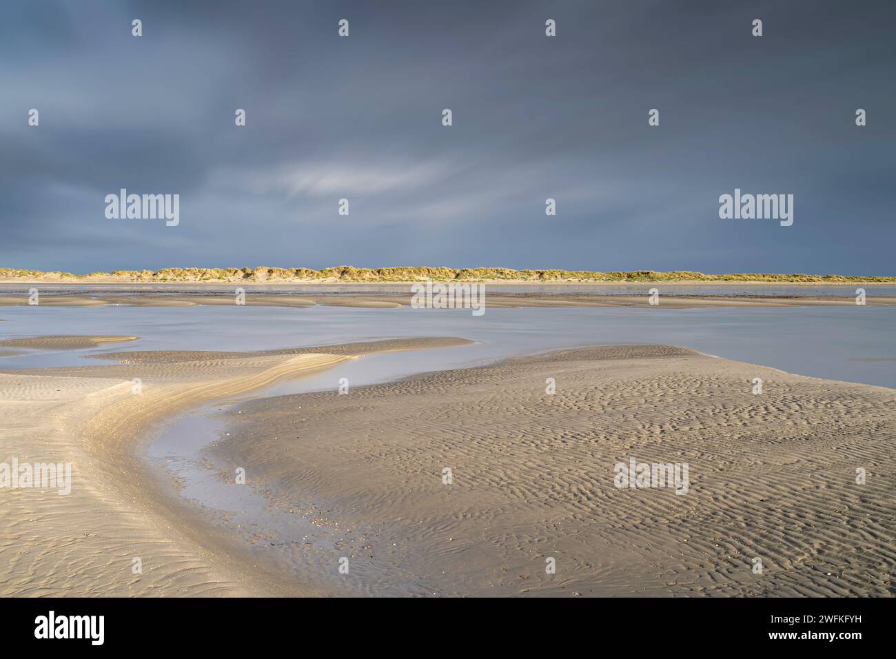 Mentre le nuvole di tempesta si accumulano sopra le dune, la splendida spiaggia di West Wittering è illuminata dal sole che rivela sabbia scolpita durante la bassa marea. Foto Stock