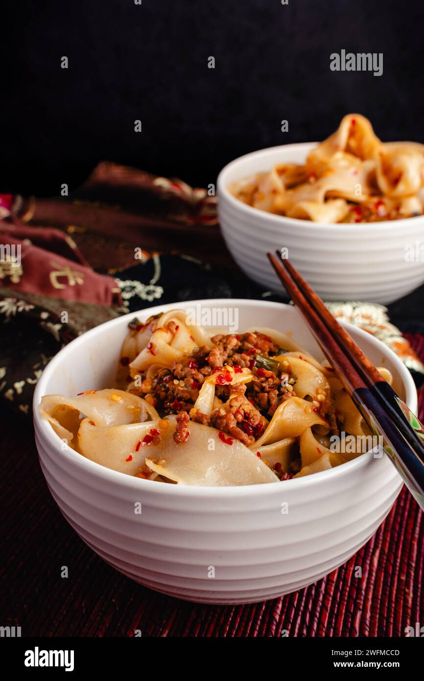 Tagliatelle di Biang Biang condite con salsa piccante all'olio di peperoncino da vicino: Biang biang mian condito con maiale macinato e olio di peperoncino servito in ciotole con bacchette Foto Stock