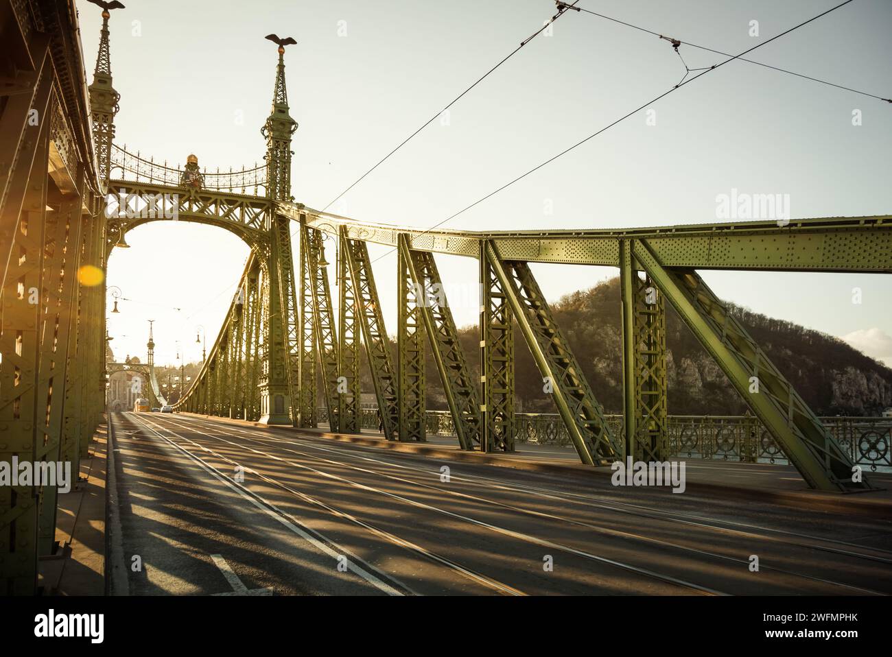 Liberty Bridge sotto il sole della sera. Vista da piazza Fővám tér sul ponte e sulla riva destra del Danubio. Sole basso e numerose ombre di capriate del ponte Foto Stock