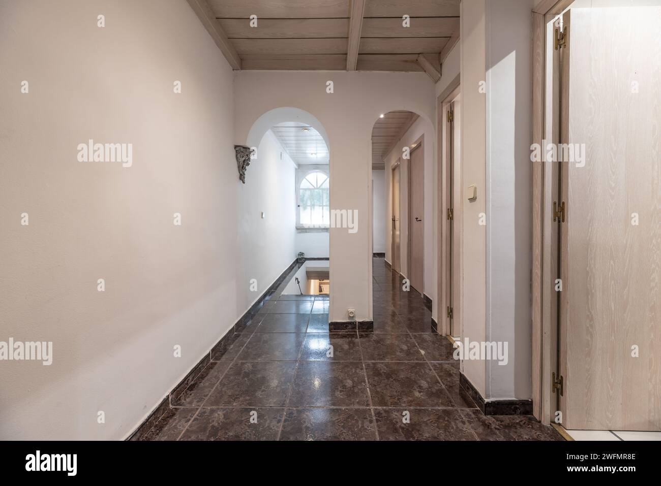 Corridoio di casa residenziale con porte in legno di quercia bianca, pavimenti in gres scuro lucido e scale che conducono al piano terra Foto Stock